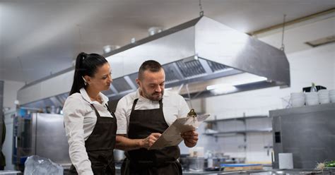A chef and cook discussing menu indoors in restaurant kitchen. photo ...