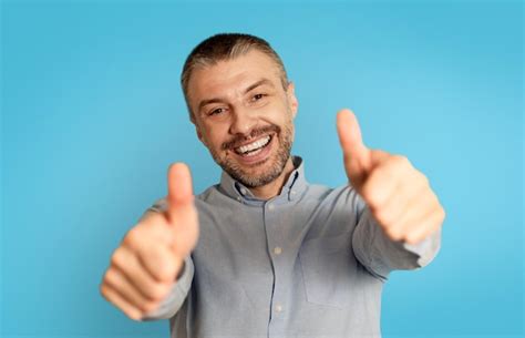 Premium Photo | Joyful Male Gesturing Thumbs Up With Both Hands Blue ...